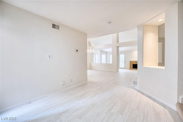 spare room featuring baseboards, visible vents, a tiled fireplace, and an inviting chandelier