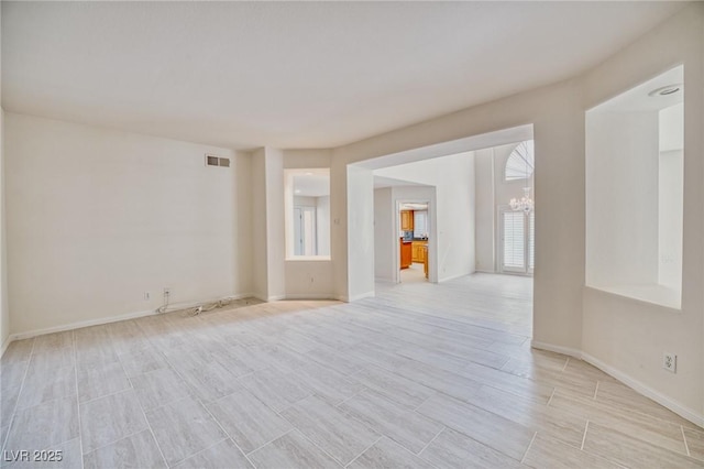 empty room with baseboards, visible vents, a notable chandelier, and wood finish floors