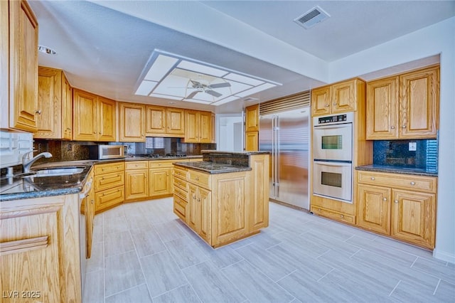 kitchen featuring visible vents, dark stone counters, appliances with stainless steel finishes, a center island, and a sink