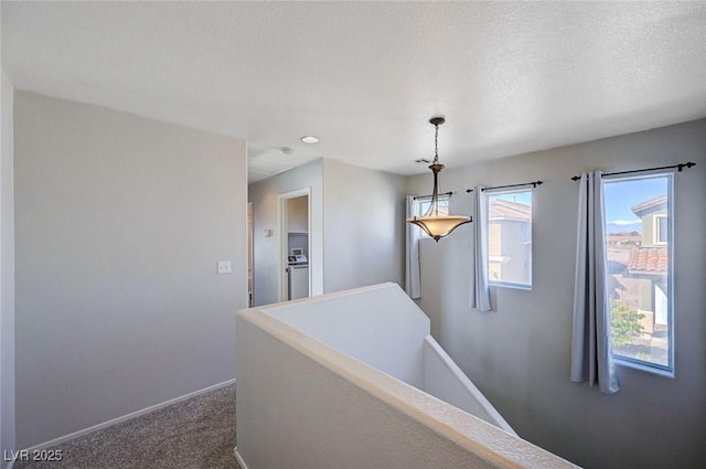 corridor with dark carpet, a textured ceiling, an upstairs landing, washer / dryer, and baseboards