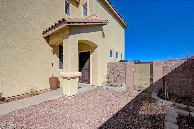 view of exterior entry featuring a tile roof, a gate, fence, and stucco siding