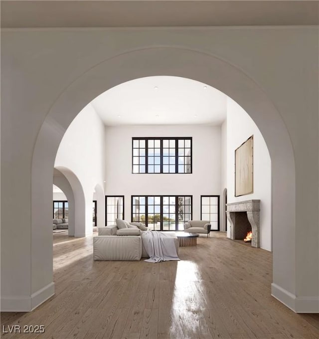 unfurnished living room featuring baseboards, arched walkways, wood finished floors, a lit fireplace, and a high ceiling