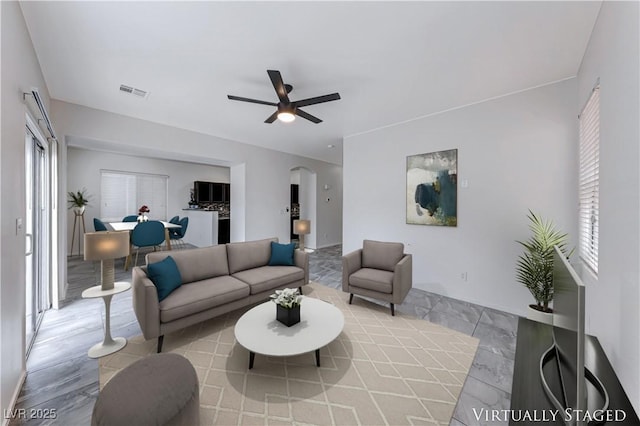 living area featuring arched walkways, visible vents, and a ceiling fan