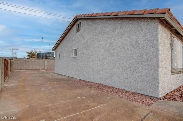 view of side of property featuring a tiled roof, a patio area, a fenced backyard, and stucco siding