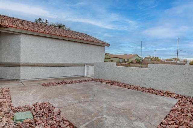 view of side of property featuring fence private yard, a patio area, a tile roof, and stucco siding