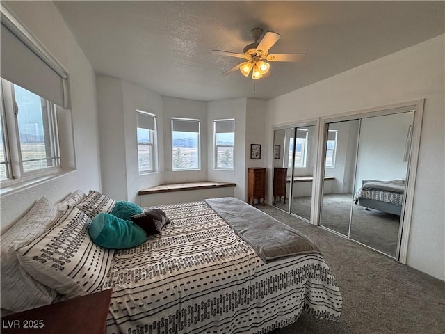 carpeted bedroom with a textured ceiling, two closets, and a ceiling fan