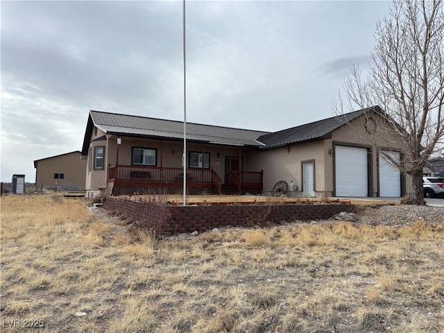 ranch-style home featuring a porch, stucco siding, a garage, and metal roof