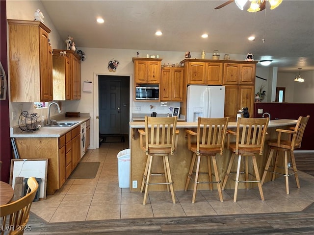 kitchen featuring white refrigerator with ice dispenser, brown cabinetry, stainless steel microwave, light countertops, and a sink