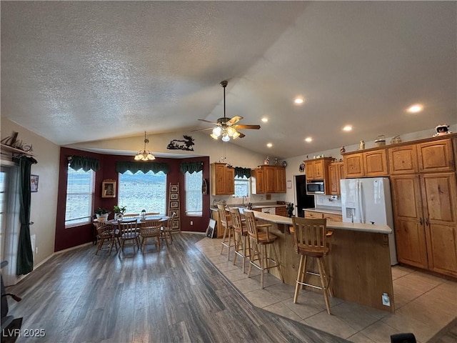 kitchen with light countertops, a large island, brown cabinetry, stainless steel microwave, and a kitchen bar