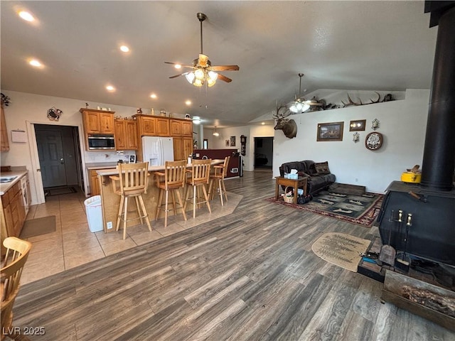 dining space with a ceiling fan, lofted ceiling, a wood stove, and light wood-style floors