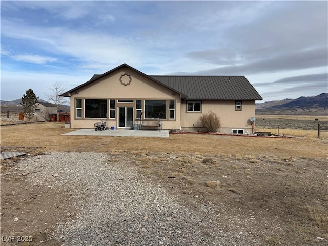 back of house with stucco siding, fence, a mountain view, metal roof, and a patio area