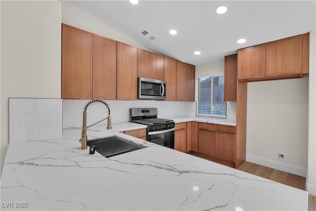 kitchen with a sink, visible vents, appliances with stainless steel finishes, brown cabinets, and decorative backsplash