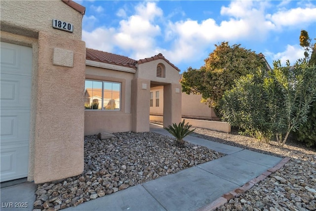 property entrance featuring a tiled roof, an attached garage, and stucco siding