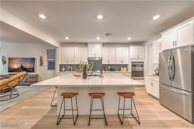 kitchen featuring an island with sink, light stone countertops, white cabinets, and stainless steel appliances