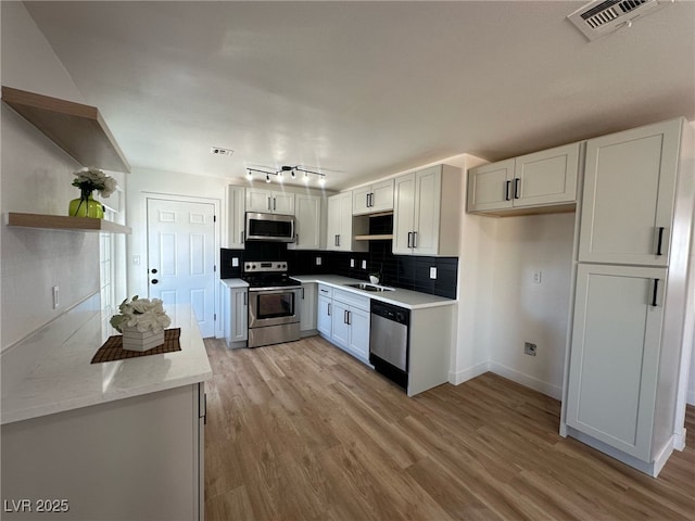 kitchen with light wood-style flooring, stainless steel appliances, a sink, white cabinetry, and backsplash