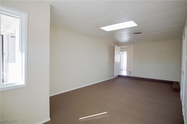 unfurnished room featuring dark colored carpet, a drop ceiling, visible vents, and baseboards