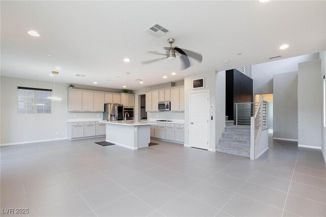 kitchen featuring stainless steel appliances, visible vents, open floor plan, light countertops, and a center island with sink