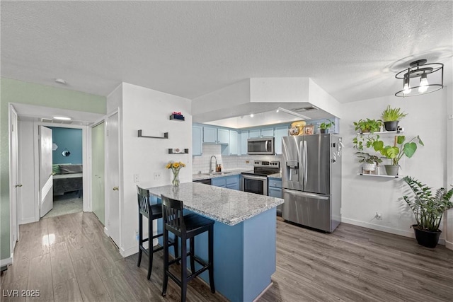 kitchen featuring appliances with stainless steel finishes, a breakfast bar area, a peninsula, blue cabinetry, and a sink