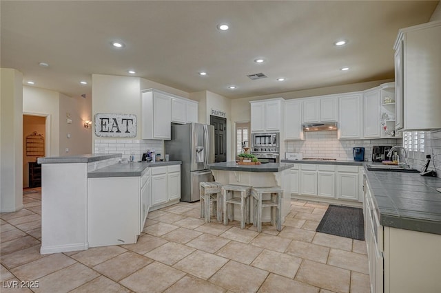 kitchen with appliances with stainless steel finishes, white cabinetry, a kitchen island, under cabinet range hood, and a kitchen bar