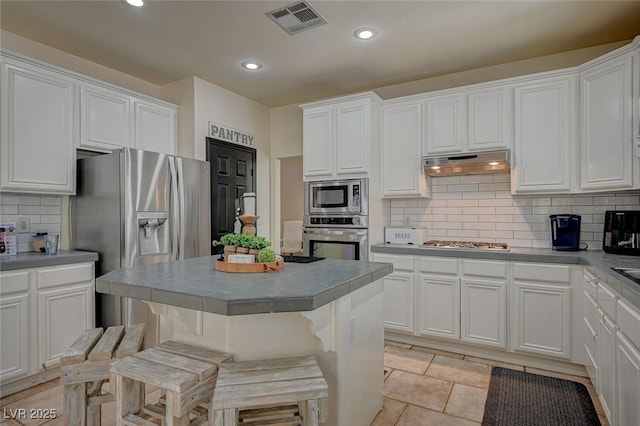 kitchen with visible vents, white cabinets, appliances with stainless steel finishes, a breakfast bar area, and under cabinet range hood