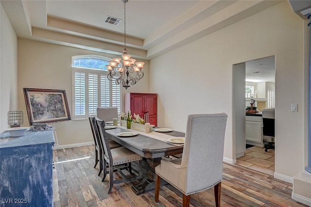 dining space featuring an inviting chandelier, visible vents, a raised ceiling, and wood finished floors