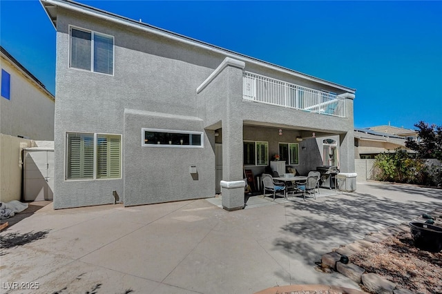 rear view of house featuring a patio area, fence, a balcony, and stucco siding