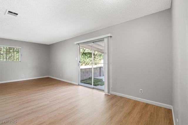 spare room with light wood-style floors, a wealth of natural light, visible vents, and baseboards