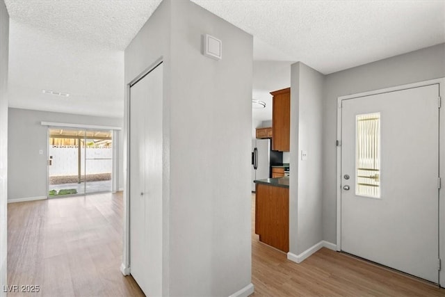 foyer entrance featuring baseboards, a textured ceiling, and light wood finished floors