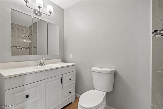 bathroom featuring tiled shower, vanity, toilet, and baseboards