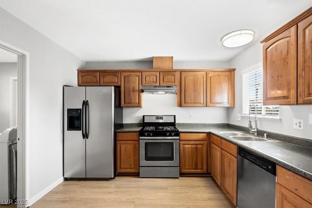 kitchen with stainless steel appliances, dark countertops, light wood-style flooring, a sink, and under cabinet range hood