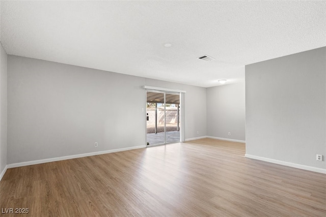 empty room featuring a textured ceiling, light wood finished floors, visible vents, and baseboards