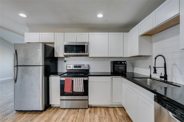 kitchen with light wood-style flooring, a sink, white cabinets, appliances with stainless steel finishes, and dark countertops