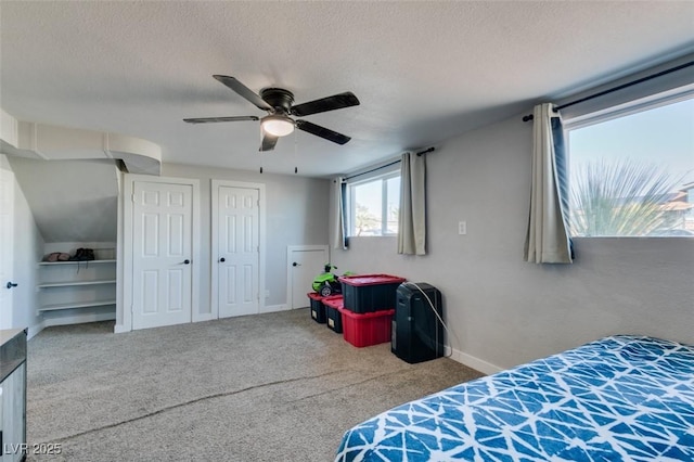 carpeted bedroom featuring multiple closets, a textured ceiling, baseboards, and a ceiling fan