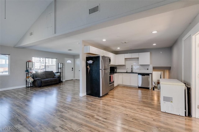 kitchen featuring dark countertops, appliances with stainless steel finishes, open floor plan, white cabinetry, and light wood-type flooring