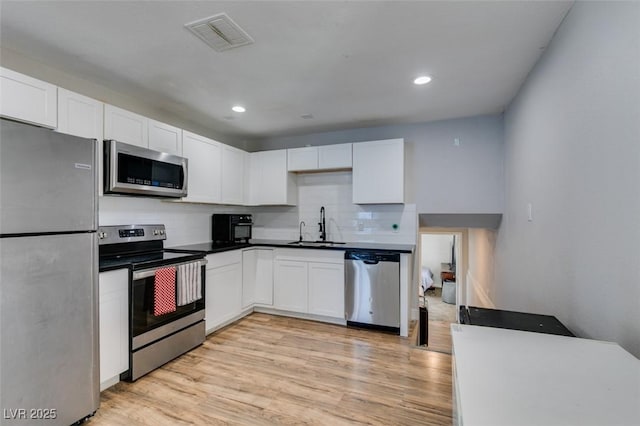 kitchen with stainless steel appliances, visible vents, white cabinetry, a sink, and light wood-type flooring