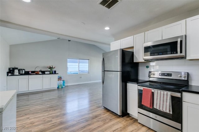 kitchen featuring dark countertops, lofted ceiling, visible vents, appliances with stainless steel finishes, and white cabinetry