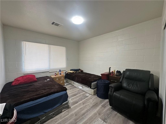 bedroom featuring light wood-type flooring, visible vents, and concrete block wall