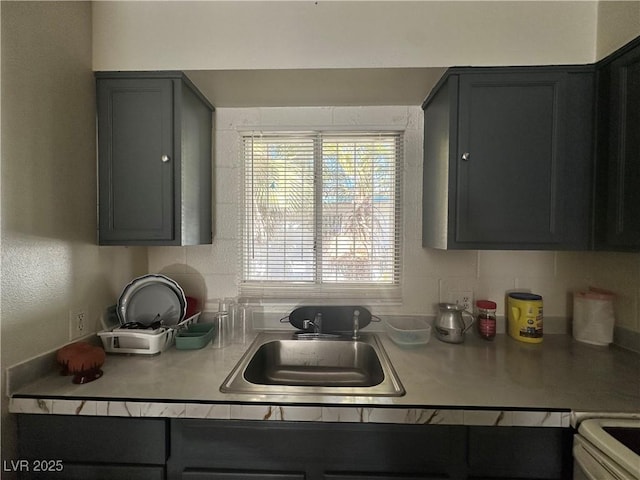 kitchen with stove, gray cabinets, a sink, and light countertops