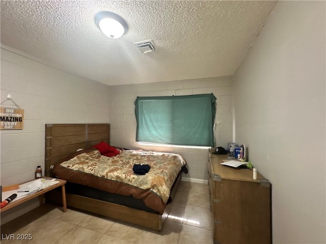 bedroom with concrete block wall, visible vents, and a textured ceiling