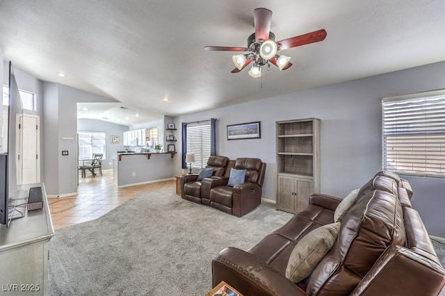 living room featuring lofted ceiling, light tile patterned flooring, light colored carpet, a ceiling fan, and baseboards