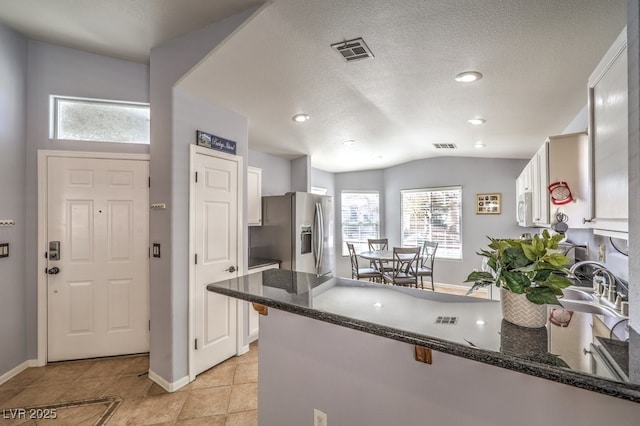 kitchen featuring visible vents, white microwave, a peninsula, stainless steel refrigerator with ice dispenser, and a sink