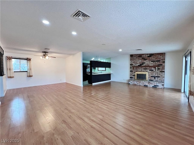 unfurnished living room featuring visible vents, a fireplace, a textured ceiling, and light wood finished floors