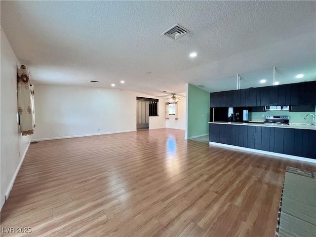 unfurnished living room featuring visible vents, ceiling fan, a textured ceiling, light wood-type flooring, and a sink