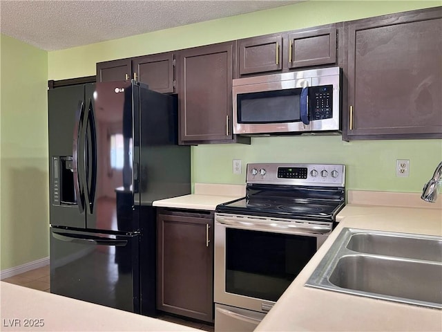 kitchen with appliances with stainless steel finishes, light countertops, a sink, and dark brown cabinetry