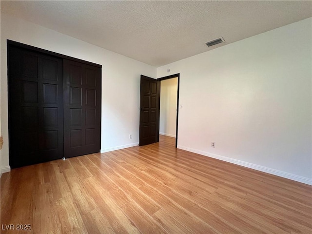 unfurnished bedroom featuring baseboards, visible vents, a textured ceiling, light wood-type flooring, and a closet