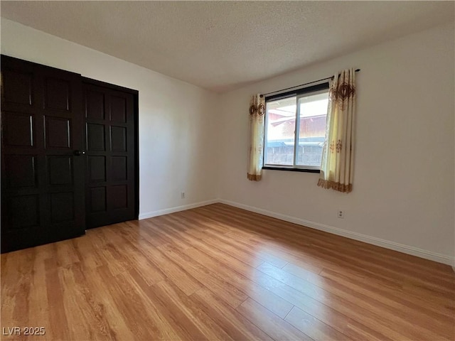 unfurnished bedroom featuring a textured ceiling, light wood finished floors, and baseboards