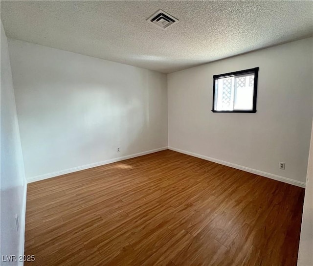 unfurnished room with visible vents, a textured ceiling, baseboards, and wood finished floors