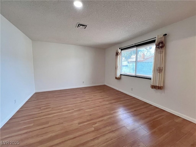 unfurnished room featuring a textured ceiling, light wood-style flooring, visible vents, and baseboards