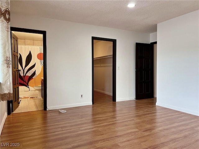 unfurnished bedroom with a textured ceiling, a walk in closet, light wood-style flooring, and baseboards