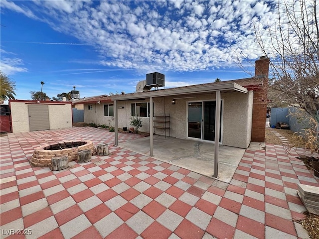 back of house with a fire pit, an outbuilding, a shed, central AC, and stucco siding